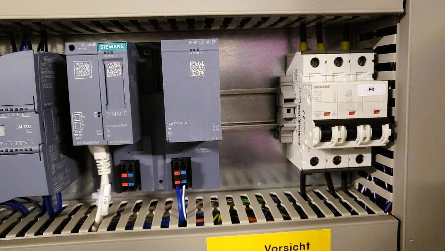 WI Automtisierungstechnik GmbH - Industrielle Automatisierung - Ansicht eines Ausschnitts eines elektrischen Schaltschranks mit Siemens-SPS-Modulen und weißen Leistungsschaltern auf der rechten Seite.