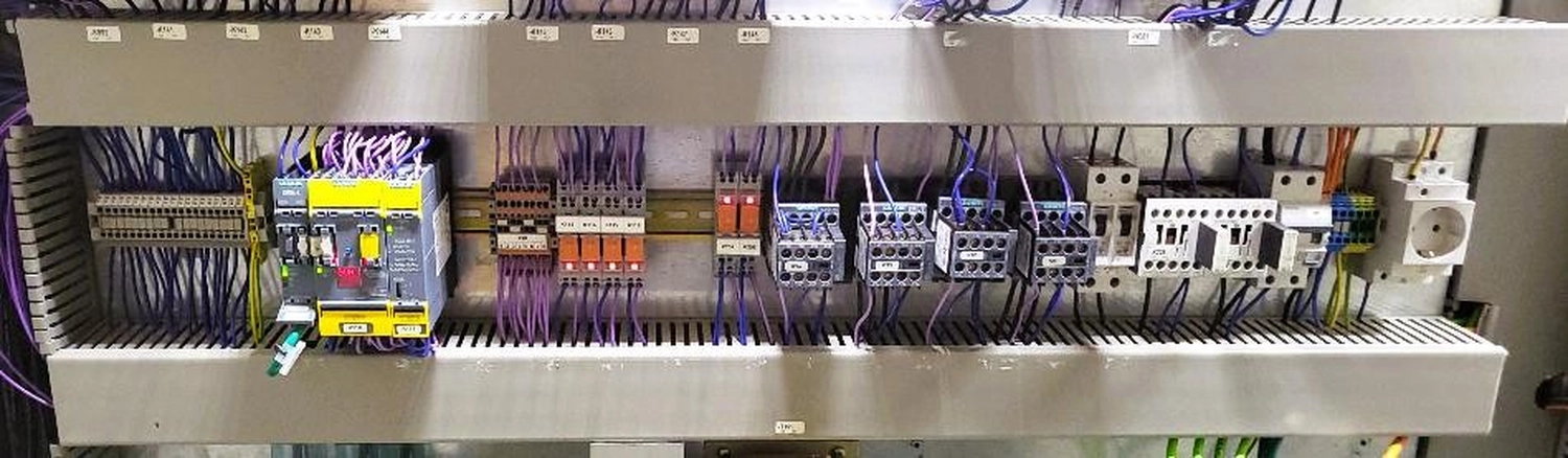 WI Automtisierungstechnik GmbH - Industrielle Automatisierung - Nahaufnahme eines offenen industriellen elektrischen Schaltschranks, der mit verschiedenen Komponenten gefüllt ist, darunter Klemmenblöcke, Relais, Leistungsschalter und violette Kabel.