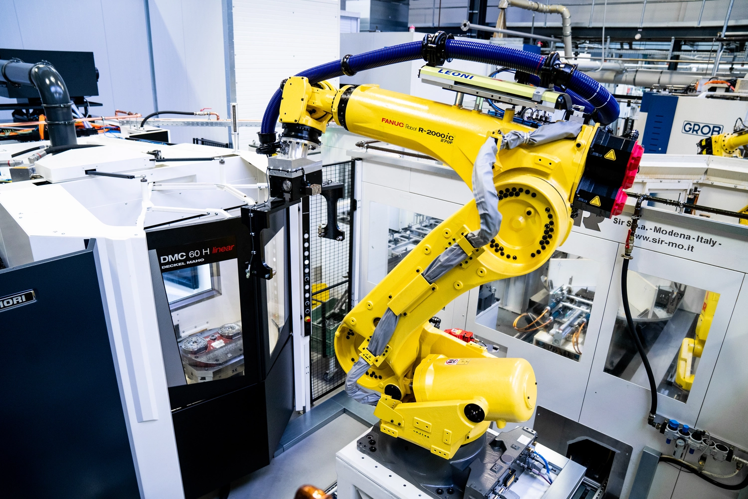 WI Automtisierungstechnik GmbH - Industrielle Automatisierung - Ein gelber Industrieroboterarm ist in einer Fertigungszelle im Einsatz und befindet sich neben einer Maschine mit der Bezeichnung „OMO 6014“ sowie weiteren Anlagen in einer modernen Fabrikumgebung.
