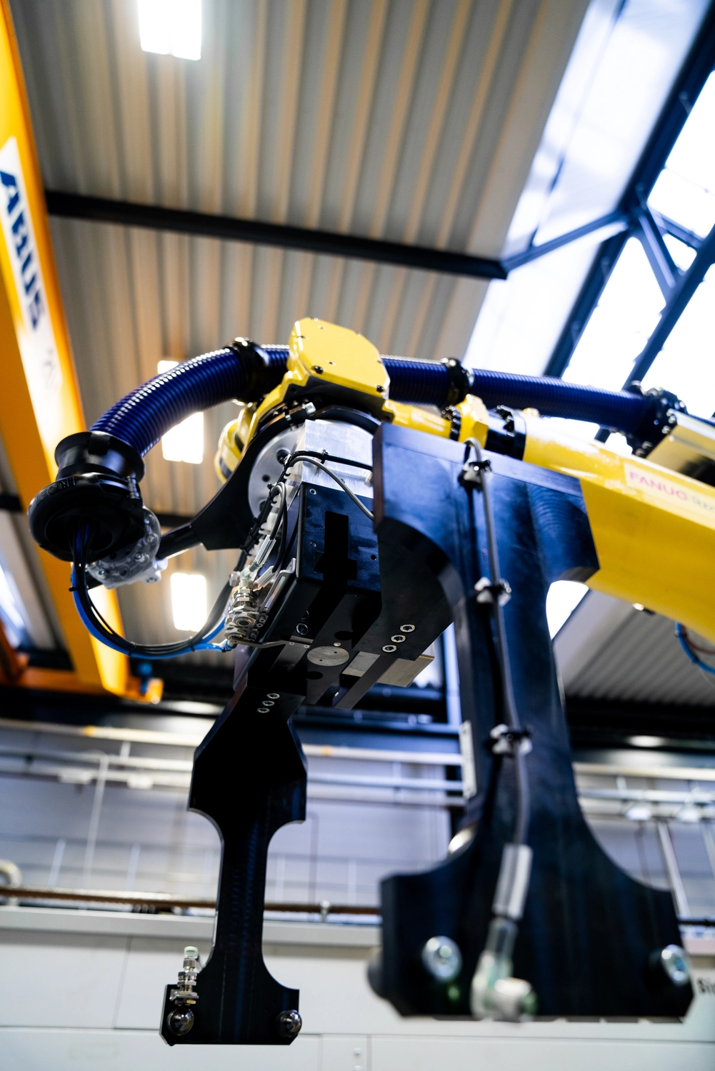 WI Automtisierungstechnik GmbH - Industrielle Automatisierung - Ein gelb-schwarzer ABB-Industrieroboterarm mit angebrachtem Greiferwerkzeug ist in einer Fabrikumgebung im Einsatz. Der Arm weist blaue Kabel auf, und auf einer vertikalen Trägerstruktur ist der Schriftzug „ABUS“ sichtbar.