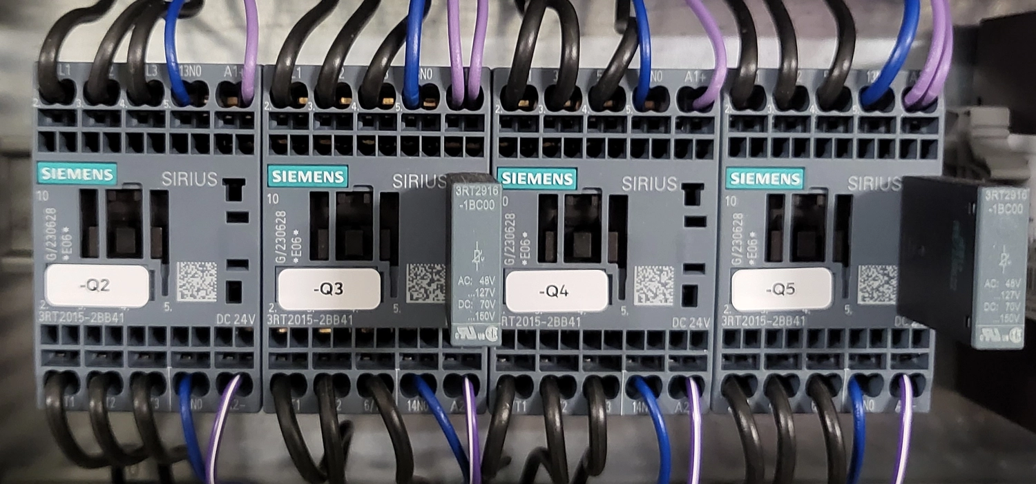 WI Automtisierungstechnik GmbH - Industrielle Automatisierung - Eine Reihe grauer Siemens SIRIUS 3RT2015-2BB41 Motorstarter und ein grünes Sicherheitsrelais, beschriftet mit "-Q3", "-Q4" und "-Q5", mit verschiedenfarbigen Drähten, die an ihre Klemmen angeschlossen sind.